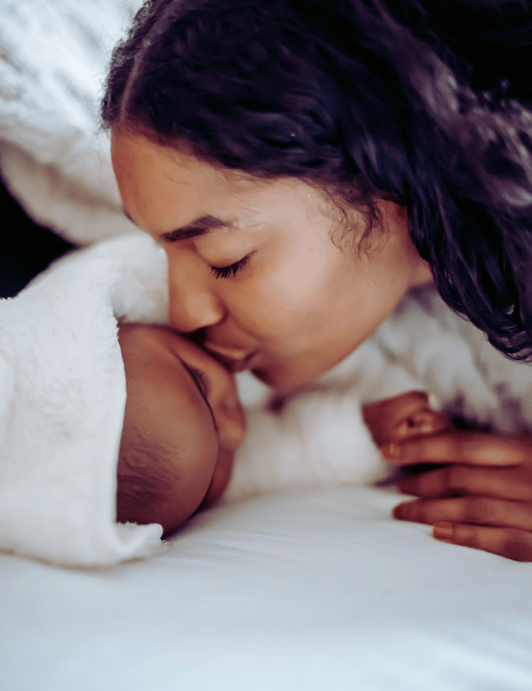 Woman lying on a bed kissing sleeping baby on the cheek
