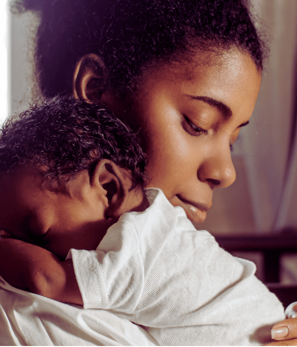 Woman holding a baby close together, both wearing white clothing.