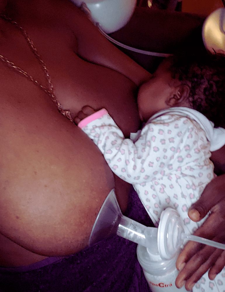 Person using a breast pump while nursing a baby, set against a blurred indoor background