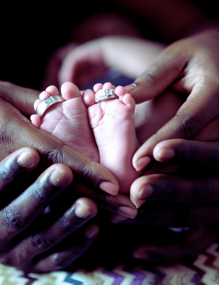 Two pairs of hands holding a pair of baby feet with rings on.