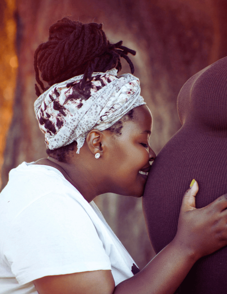 Woman with braided hair wearing a headscarf, holding a mama's pregnant belly