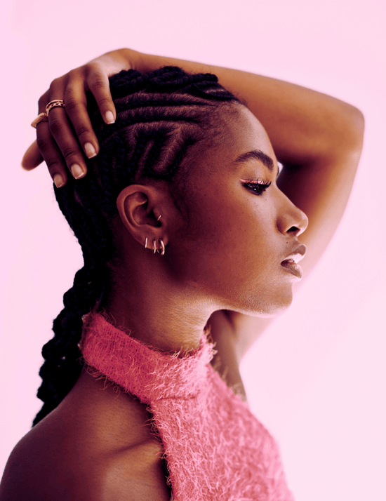 Woman with braided hair wearing a pink top against a light pink background