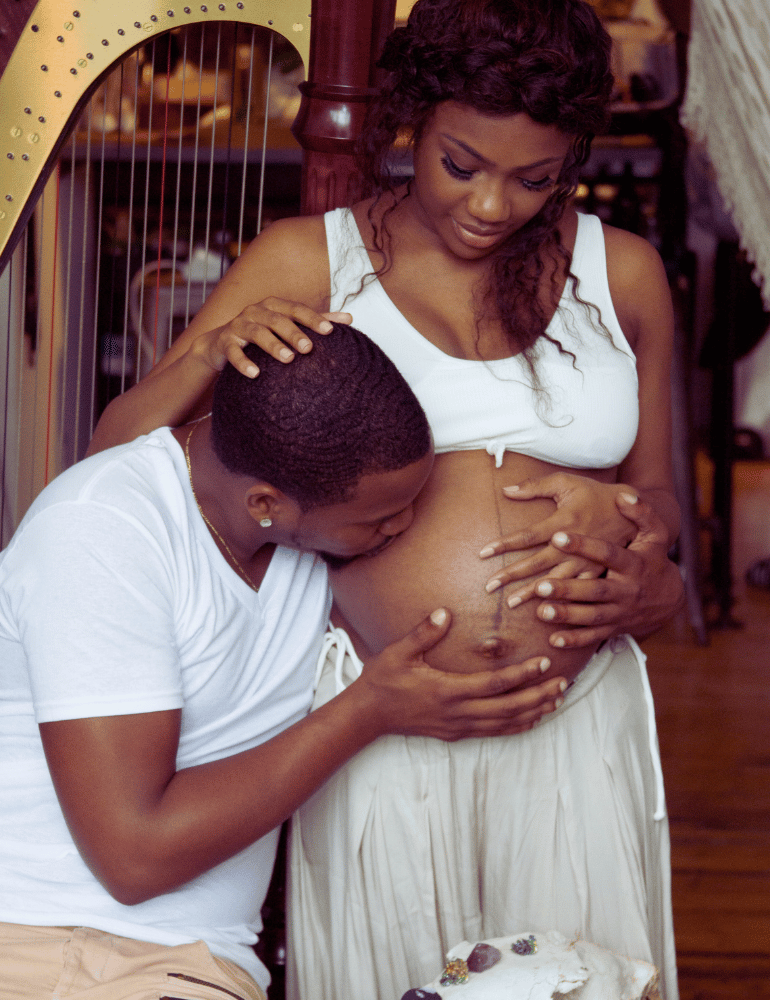 Man and woman embracing, with the woman pregnant, in a warm indoor setting.