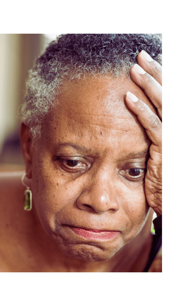 Close-up of a person with gray hair holding their head, with a blurred background