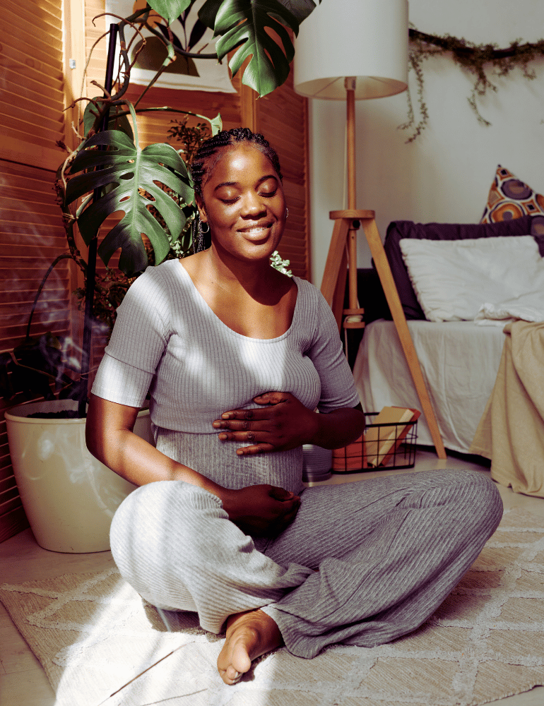 Woman sitting on the floor in a cozy living room with plants and a lamp.